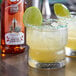 A glass of Master of Mixes Agave Syrup with a lime wedge and a sugar rim on a table.