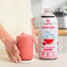 A person holding a jar of pink Smartfruit Wild Watermelon beverage next to a glass of pink liquid.