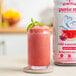 A glass of pink Smartfruit Wild Watermelon beverage next to a bottle of the mix.