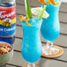 A tall glass of blue Torani Blue Curacao drink with nuts and orange slices on the side.