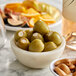 A bowl of Belosa cream cheese stuffed green olives on a table with a bottle of wine.