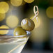 A green olive with cream cheese inside on a toothpick in a martini.