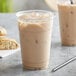 A plastic cup filled with brown Tazo Skinny Chai Tea Latte with a straw on a white background.