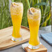 A wooden tray with two glasses of yellow Fanale Passion Fruit syrup with straws.