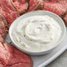 Sliced meat next to a bowl of white horseradish sauce.