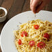 A person sprinkling coarse ground black pepper on a plate of spaghetti.