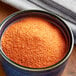 A bowl of powdered orange Goya Sazon seasoning packets on a table.