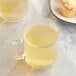 A clear glass mug filled with yellow Twinings Lemon & Ginger tea next to a muffin.