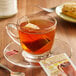 A glass cup of Bigelow hot cinnamon black tea with a tea bag on a saucer.