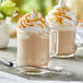 A glass mug of Capora Caramel Latte Frappe with whipped cream and caramel sauce on top.