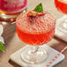A glass of red Lyre's Aperitif Rosso with a strawberry on the rim and a red and white straw.