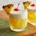 Two glasses of yellow Pina Colada drinks with cherries and pineapple on top.