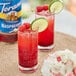 Two glasses of red drinks with lime and raspberry garnishes with a jar of raspberries in the background.