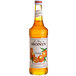 A Monin orange fruit syrup bottle filled with orange liquid.