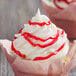A cupcake with white frosting and red drizzle using Satin Ice Red Vanilla Glitter Glaze.