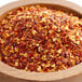 A wooden bowl filled with Regal Mild Crushed Red Pepper on a table.