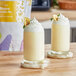 Two glasses of banana milkshakes topped with whipped cream and bananas on a wooden table.