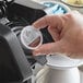 A hand placing an Ellis Colombian Coffee single serve cup into a coffee maker.