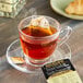 A glass cup of French Vanilla tea with a Bigelow French Vanilla tea bag on a saucer.