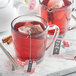 A glass mug of red Numi Organic Hibiscus tea with a tea bag in it.