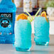A glass of blue Lotus Plant Power Energy Concentrate with a straw and an orange slice.