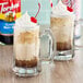 Two glass mugs filled with root beer floats with whipped cream and straws.