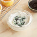 A cupcake with green and white swirled frosting next to a bowl of chocolate sauce.