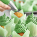 A hand using Chefmaster Leaf Green Gel Food Coloring to decorate cupcakes with green frosting.