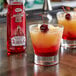 Two glasses of red drinks with Master of Mixes Grenadine Syrup on a bar counter.