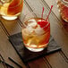 A wooden table with a glass of ice and a cherry on top of a drink.