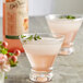 Two glasses of pink drinks garnished with leaves and flowers on a table.