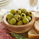 A bowl of Frutto d'Italia pitted green olives on a table with bread and meat.