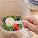 A hand holding a plastic spoon filled with Add A Scoop Pea Protein powder over a blender.