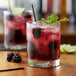 A glass of red liquid flavored with Monin Wild Blackberry Syrup and garnished with berries and ice.