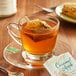 A glass cup of Bigelow Caramel Apple Tea with a tea bag in it on a table with a plate of pastries.