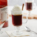 A glass of coffee with whipped cream and cinnamon with a bottle of DaVinci Gourmet Cinnamon Bark Syrup on the table.