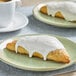 A plate with a pastry with white icing and a white cup of coffee.
