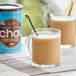 A glass mug of brown David Rio Elephant Vanilla Chai tea on a table with a can of chai.