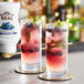 Two glasses of blueberry drinks garnished with mint and blueberries on a table with a bottle of Real Blueberry Puree Infused Syrup.