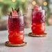 A close-up of two red and pink Tiki Breeze drinks with fruit on the rim.