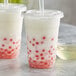 A plastic cup with white liquid and red dots with a straw.