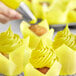 A hand using yellow Chefmaster food coloring to decorate a cupcake with yellow frosting.