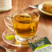 A glass cup of Bigelow Earl Grey Green Tea with a Bigelow tea bag on a saucer.