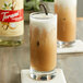 A glass of iced coffee with Torani vanilla syrup on a white background.