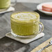 A clear glass cup filled with green tea latte made from green tea powder mix, placed on a marble coaster.