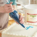 A person decorating a cake with blue Lucky Leaf piping gel in a blue bag.