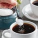 A hand holding a spoon with Splenda Monk Fruit sweetener in a cup of coffee.