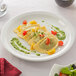 A plate of ravioli with basil sauce, tomatoes, and cheese on a table with a red cloth.