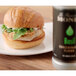 A sandwich on a plate next to a bottle of Monin Basil Concentrated Flavor.