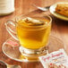 A glass cup of Bigelow Ginger Snappish Herbal Tea with a tea bag in it on a saucer with a spoon.